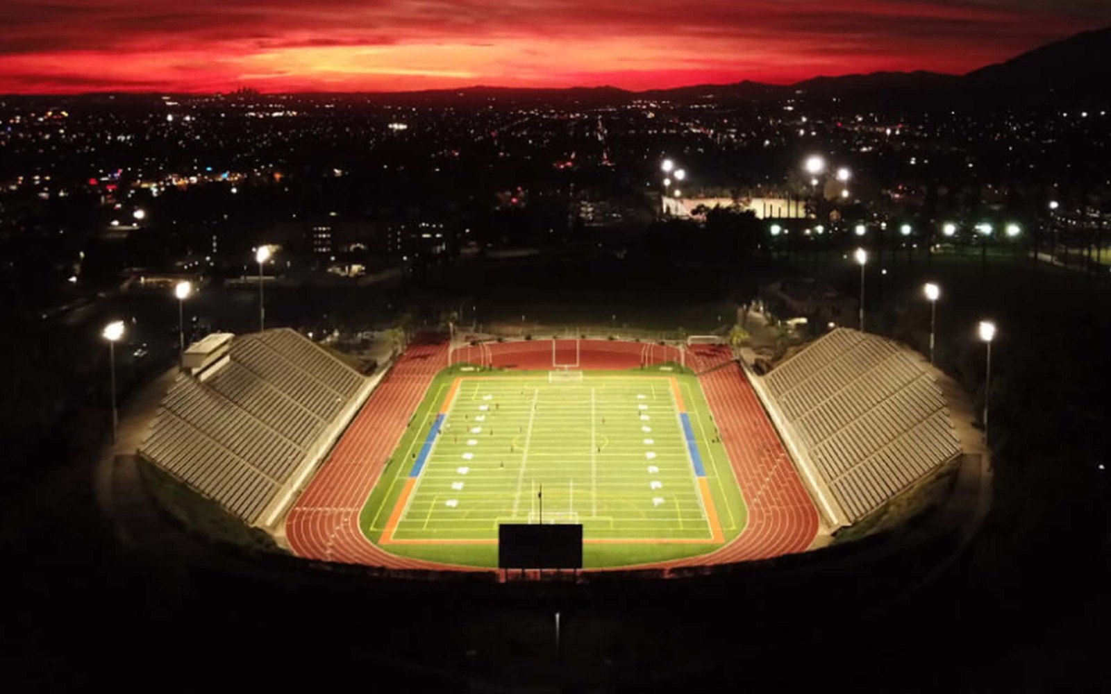 Aerial view of a lit football stadium and running track at dusk