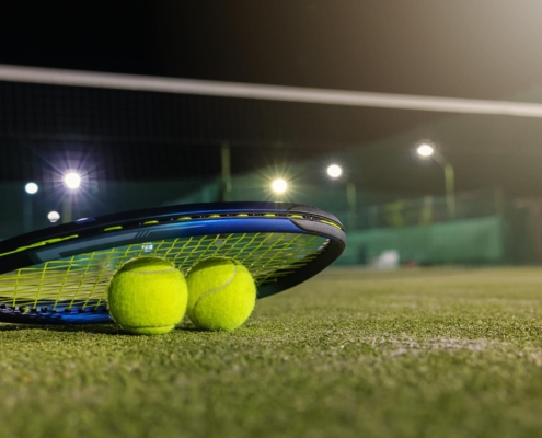 Image of a racket and balls laying on a tennis court being lit up at night.