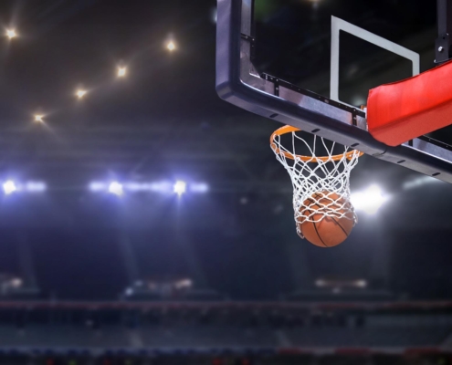Side view of a basketball going through a hoop with arena lights shining in the back